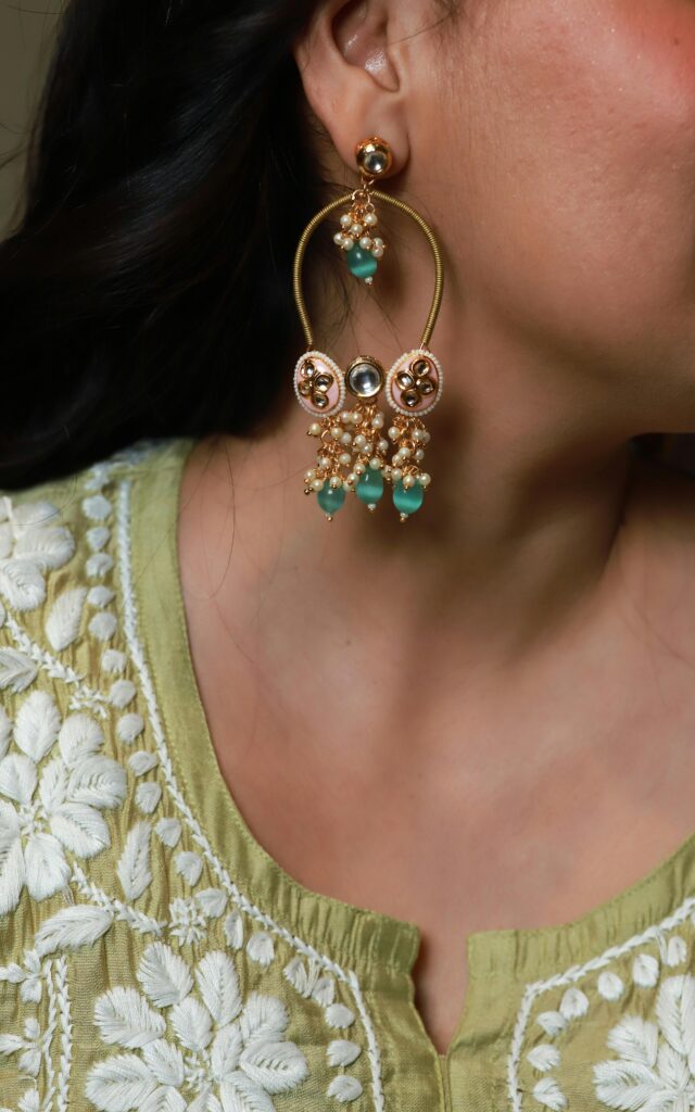 Close-up of an elegant gold and turquoise designer earring paired with a floral embroidered top.